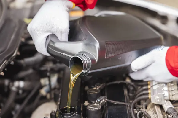 Close up Car Mechanic Pouring Oil during Oil Change. A mechanic in a uniform and gloves pours synthetic oil into the engine