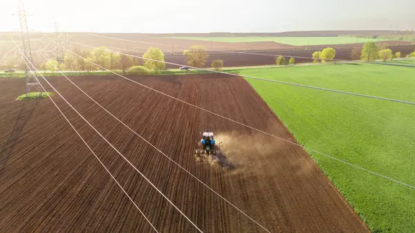 播种的工作 拖拉机在春天犁田 空中俯瞰 电力线路在前景中 图库图片