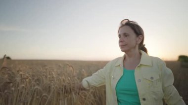 Agronomist tarlada yürüyor ve buğday hasadının tadını çıkarıyor, yaz hasadını kontrol eden kadın. Toptan tahıl ticareti..