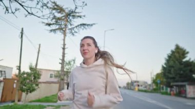 Bahar şehrinde koşan sportif bir kızın portresi, sağlıklı bir yaşam tarzı. Kulaklık takan, gülümseyen ve ağır çekimde koşan genç spor kadın.