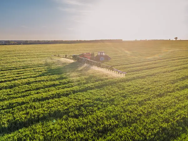 Çağdaş traktör yemyeşil bir tarlada tarım ilacı ya da gübre püskürtüyor. Eylem halindeki tarım makineleri sürdürülebilir tarım ve gıda üretimini temsil ediyor.