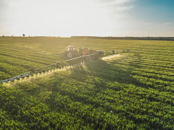 Modern traktörün hava görüntüsü yeşil bir alana böcek ilacı ya da gübre püskürtüyor.