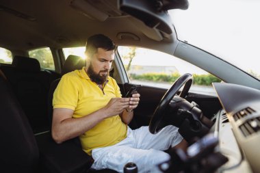 Erkek sürücü güneşli bir günde cep telefonunu kontrol ediyor. 