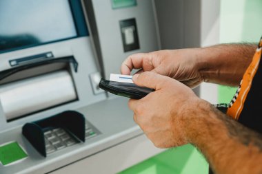 Erkek ATM kartı. ATM giriş kartı. Adam cüzdanını tutarken kredi kartını ATM 'ye koyuyor..