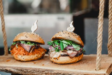 Ahşap bir üste lezzetli hamburgerler. Eski ahşap bir masada iki lezzetli ev yapımı sığır eti, peynir ve sebze. Yağlı, sağlıksız yiyecekler. Hamburger Festivali.