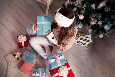 Noel ağacının önünde hediyeleri olan mutlu bir kadın. Şenlik odasında, örgü süveter giymiş şık bir kadın hediye tutuyor. Mutlu Noeller ve mutlu Noeller Yeni yıl ve Noel konsepti