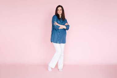 Kendine güveni tam, rahat giyinen, elleri pembe arkaplan önünde duran, profesyonel profil ya da web sitesi afişi için tüm vücudunu çeken iş kadını.