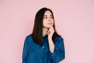 Dinginlik ve Düşünce: Çenesinde Elle Güzel Bir Kızın Düşünceli Portresi, Boş Alan 'a Bakıyor, Sakinleştirici Pembe Bir Arkaplanda İzole Edilmiş.