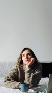 Evde çalışan yaratıcı bir kadın öğrenciler için ders planı ve program hazırlıyor, dizüstü bilgisayar kullanıyor ve mutfak masasında kahve içiyor. Üretken öğretmen dizüstü bilgisayarda özet ve program yazar..