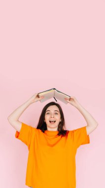 Joyful Book Enthusiasm: Cheerful Woman Holding Book Overhead with Exuberance - Delightful Mood and Positivity Concept, Isolated on Pink Background clipart