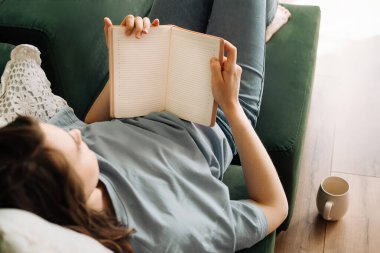 - Boş zaman. Kitap, Yemek ve Oturma Odası Kanepesinde Çay İçen Genç Kadın. Evde Rahat Okuma ve Yeme: Kitap, Yiyecek ve İçecek ile Rahat Yaşam Tarzı. Yurtiçi Konforda Rahatlama.