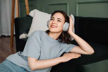 Düşünceli, neşeli, kablosuz kulaklık takan, boş zamanlarında müzik dinleyen genç bir kadın. Müzikal Dinginlik. Kablosuz Kulaklıkla Neşeli Anları Kucaklayan Genç Kadın.