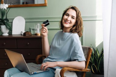 Çevrimiçi Alışveriş Joy. Kredi kartı ve dizüstü bilgisayardan memnun genç bayan. Neşeli Kadın Kredi Kartı ve Bilgisayarla İnternetten Alışveriş Yapıyor. Mutlu Alışverişçiler.