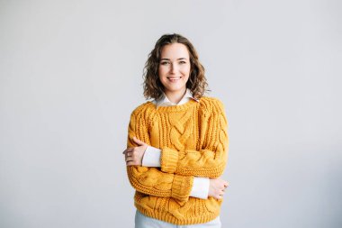 Kameraya gülümseyen kıvırcık saçlı mutlu, kendine güvenen genç bir kadın. Beyaz bir arka planda izole edilmiş, reklam, promosyon ve ticari kullanım için mükemmel. Parlak ve neşeli dikey portre.