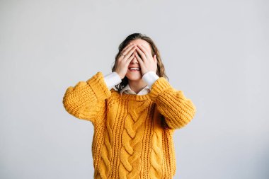 Genç yetişkin, gülümseyen, güzel, pozitif bir kadın model elleri kapalı, gözleri kapalı, beklenti içinde. Bir sürpriz ya da hediye bekliyor. Beyaz bir arka planda izole edilmiş bir sırrı tahmin ediyor..