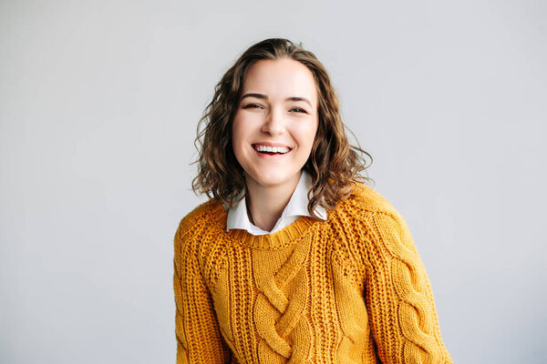 Очаровательная молодая женщина с вьющимися волосами, улыбающаяся и смотрящая в камеру. Она излучает позитив и радость, стоя изолированно на белом фоне на портрете крупного плана.