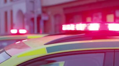 Şehir caddesinde kırmızı ve mavi ışıklı ambulans, acil müdahale için hazır. Sarı ve yeşil renkteki araçlar, aciliyetini ve önemini vurgulayarak öne çıkıyor.