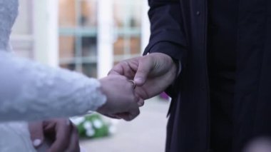 Alyans takası anını yakalayan yakın çekim. Gelinin eli dantel bir kolla süslenir, bir yüzük alır, çiçek arkaplanına yaslanır. Düğün ve romantizm için mükemmel