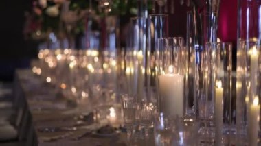 Çok güzel dekore edilmiş bir masa. Uzun vazolarda renkli çiçekler ve cam tutacaklarda mumlar var. Düğünler, ziyafetler ve resmi etkinlikler için mükemmel..