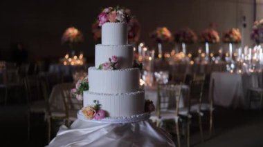 Çiçek desenli zarif düğün pastası. Masada pembe ve şeftali çiçekleriyle süslenmiş dört katlı beyaz bir düğün pastası. Sıcak ışıklandırma romantik bir karşılama ortamı yaratır.