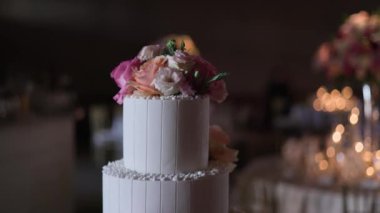 Güzel dekore edilmiş iki katlı beyaz pasta pembe ve şeftali rengi güller ve beyaz krema detaylarıyla, sıcacık, şenlikli arka planda bokeh ışıklarıyla. Düğünler ve kutlamalar için mükemmel.