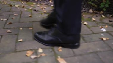 Cilalı siyah ayakkabılı bir adamın yosun kaplı tuğla bir yolda yürüdüğü yakın plan. Mevsimler, zarafet ya da açık hava hareketleri gibi kavramlar için idealdir..