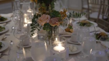Resmi bir etkinlik için çok güzel hazırlanmış bir yemek masası. İçinde mumlar, zarif cam süsler ve çiçekli süsler var. Güzel porselen tabaklar üzerinde taze salatalar sofistike bir dokunuş ekler. Düğün resepsiyonları ve ziyafetler için ideal.