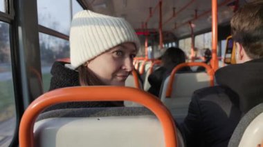 Beyaz şapkalı ve siyah ceketli bir kadın, parlak bir tramvayda otururken gülümseyerek geri dönüyor. Toplu taşıma, kentsel yaşam tarzı ve samimi anlar için mükemmel..