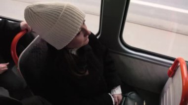 Beyaz şapkalı ve siyah paltolu bir kadın tramvayda pencerenin yanında oturur ve dışarıyı seyreder. Toplu taşıma, kentsel yaşam ve yansıtıcı anlar için mükemmel temalar.
