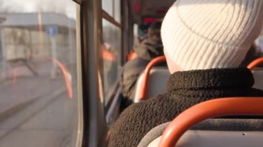 Beyaz şapkalı ve siyah ceketli bir kadın, güneş içeri girerken tramvayın camından dışarı bakıyor. Kentsel taşıma, toplu taşıma ve yansıtıcı anlar için ideal.