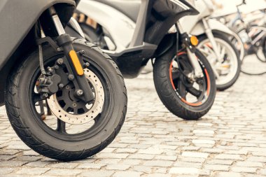Bir Avrupa şehrinde kaldırım taşı sokağına park edilmiş scooter ön tekerlerin yakın plan çekimi. Ulaşım, çevre dostu seyahat ve şehir içi ulaşım projeleri için mükemmel bir kentsel hareketlilik kavramı