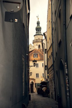 Tarihi mimarisi ve kilise kulesi olan dar bir Avrupa sokağı. Avrupa 'nın tarihi bir şehrinde, arka planda kilise kulesine giden eski binalar tarafından çerçevelenmiş büyüleyici bir kaldırım taşı sokağı.