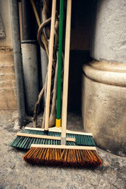 Taş bir duvara yaslanmış renkli tüylü tahta saplı süpürgeler. Temizlik, kentsel bakım ve temizlik kavramları için ideal.