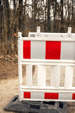 Kırmızı ve beyaz yol bariyeri bir ormanda yolu kapatıyor. İnşaat ya da güvenlik kısıtlaması doğal bir ortamda. Güvenlik, inşaat ve uyarıya bağlı görseller için ideal