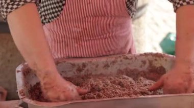 Kırmızı çizgili önlüklü bir kasap, açık hava pazarında metal bir tepside kıyma ve baharatları elle karıştırır. Gıda hazırlama görselleri, geleneksel yemek pişirme ve sokak yemekleri için ideal
