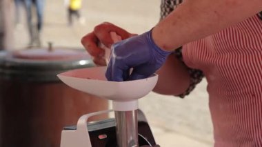 Çizgili önlüklü ve eldivenli bir kasap yemek hazırlama sırasında elektrikli öğütücüye et koyar. Görseller için mükemmel. Hijyen, gıda kullanımı ve profesyonel mutfak işleri üzerine odaklanmış.