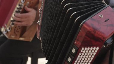 Açık havada akordeon çalan bir müzisyenin detaylı görüntüsü. El hareketlerine ve düğme detaylarına odaklan. Halk müziği, kültürel performans görselleri veya geleneksel müzik temaları için ideal