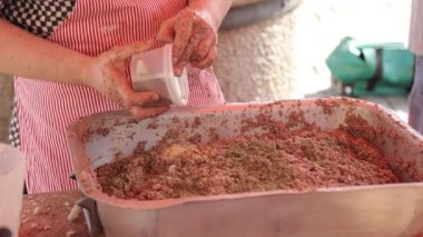 Çizgili önlüklü bir kasap, açık büfedeki büyük metal bir tepside çiğ ete baharat ekler. Hazırlık, baharat ve geleneksel et tariflerine odaklanmış görseller için mükemmel.