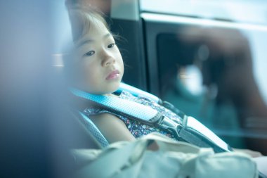 Asyalı bir çocuk çocuk çocuk koltuğunda oturuyor, kemeri arabada. Camın ön camından vurulmuş.. 