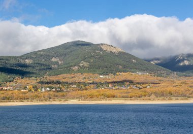 Sonbaharda Navacerrada rezervuarı, arka planda kasaba ve Madrid 'deki Sierra de Guadarrama dağları ile birlikte.