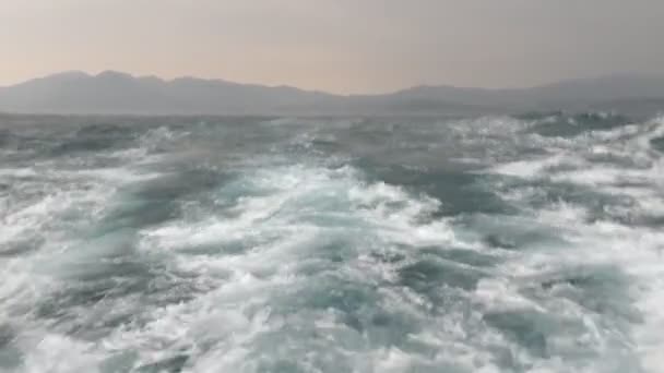从移动的船尾看 在汹涌的大海中乘风破浪 背景是群山的4K段画面 — 图库视频影像