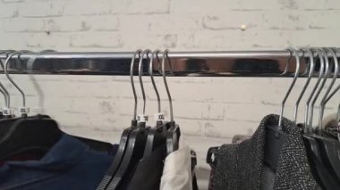 XXL kıyafetler, ikinci el mağazasındaki elbise raflarında arama, plastik askıların 4k detayları.