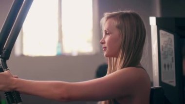 Beyaz spor gömlekli güzel bir genç kız spor salonunda kol kasları için egzersiz yapıyor. 4k biçiminde yüksek kaliteli atış