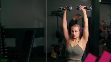 Güzel bir kadın dambılları kaldırır ve trenler nefes alır. Spor salonunda kas antrenmanı yaparken güzel bir bayan sporcunun portresi..