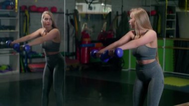 Woman exercising with dumbbells at sports ground. Young woman training muscles with dumbbells. 4K, UHD