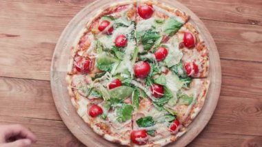Üst düzey erkek ve kadın elleri, peynirli, domatesli ve jambonlu pizza dilimleri alıyor. Bir grup aç arkadaş masada oturup ahşap masa arkasında lezzetli öğle yemeklerini paylaşıyorlar.