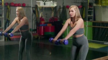 Sexy sportswoman practicing exercises with dumbbells Portrait of a concentrated woman lifting weights in a sports club.