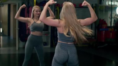 The girl poses in front of the mirror and kisses her biceps. shows his strength