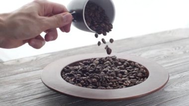A mans hand spill out roasted coffee beans from a mug into a plate. slow motion
