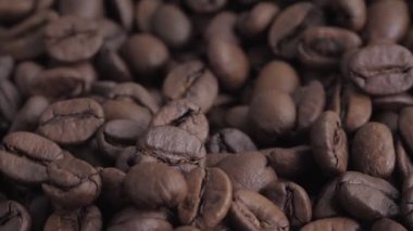 The macro of coffee beans rotates, at the bottom is the background of roasting coffee beans. The coffee bean is approaching the viewer. Selective focus